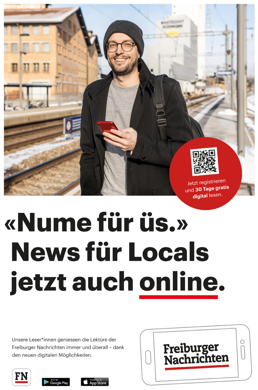 Mann mit Mobile Device am Bahnhof Düdingen. Mann mit Mantel und Kappe und Brille am Bahngleis von Düdingen.