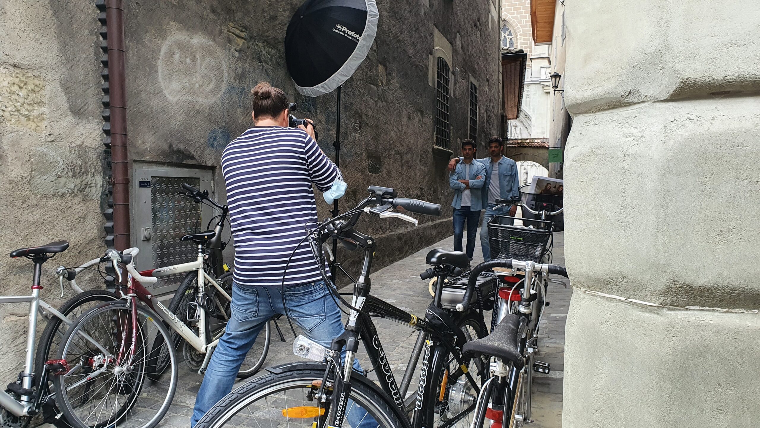 Behind the Scene Foto eines Fotoshootings. Fotograf im gestreiften Pullover fotografiert Zwillinge in einer Seitengasse in Freiburg.