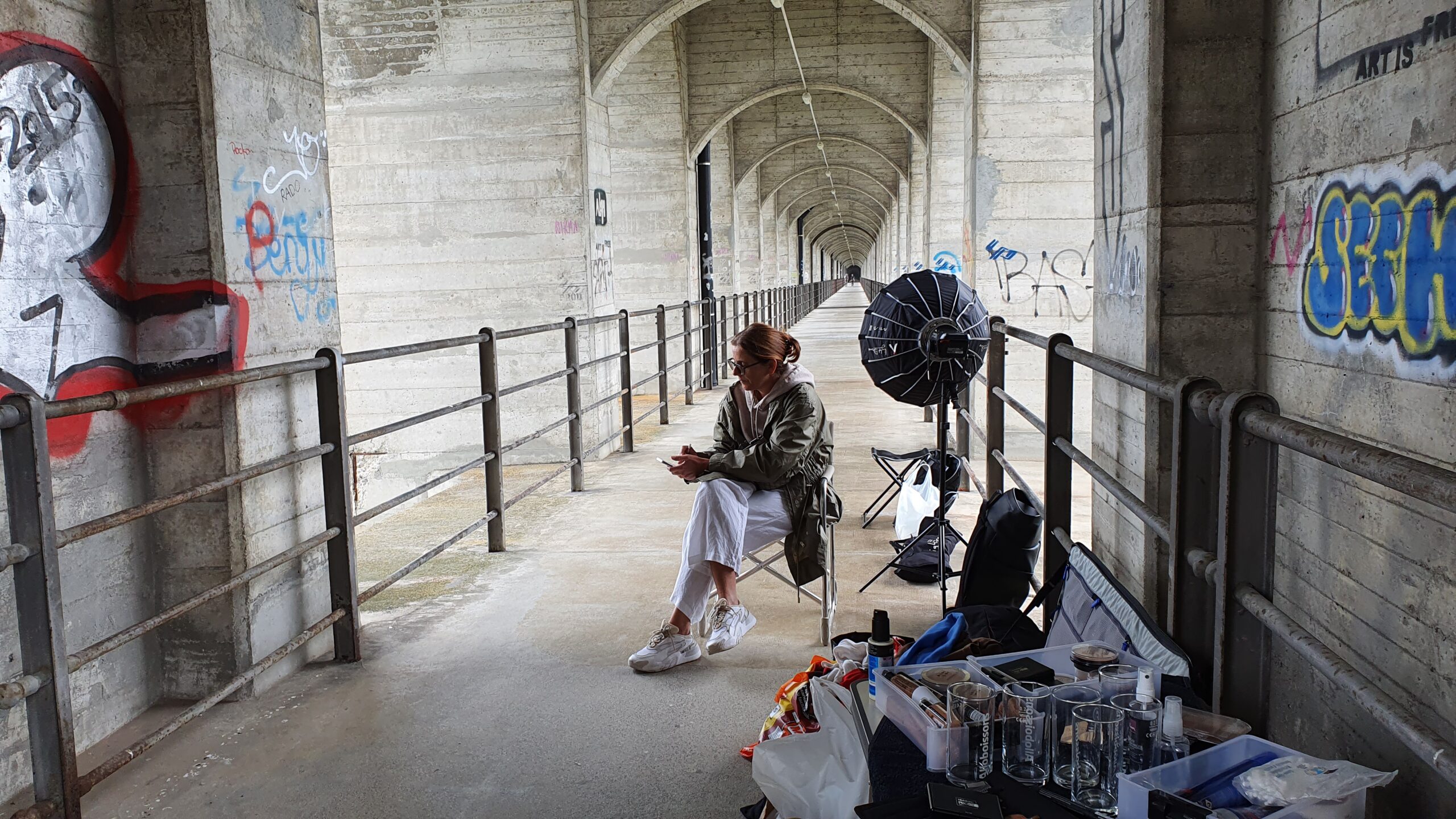 Frau sitzt auf Stuhl mit Kamera Equipment und Make Up. Warten beim Foto-Shooting auf der Grand Fey Br&uuml;cke in Freiburg.