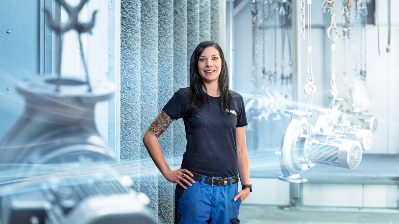 Frau in der Produktionsstätte lachend. Junge Frau mit dunkelblauem T-Shirt mit Pumpen Elementen in der Fabrikation.