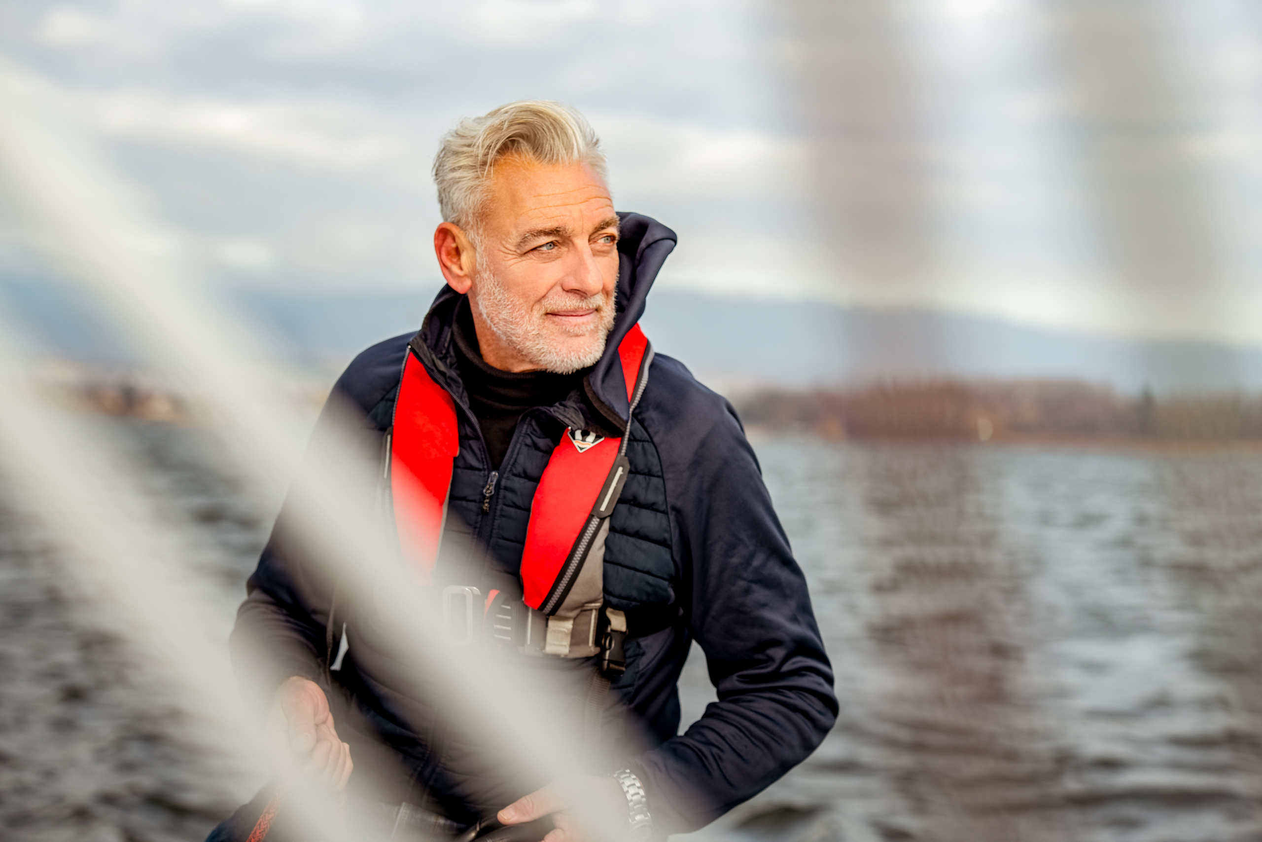 Mann am Segeln auf dem Murtensee. Mann mit weissem Haar und blauer Jacke auf dem Boot im Murtensee.
