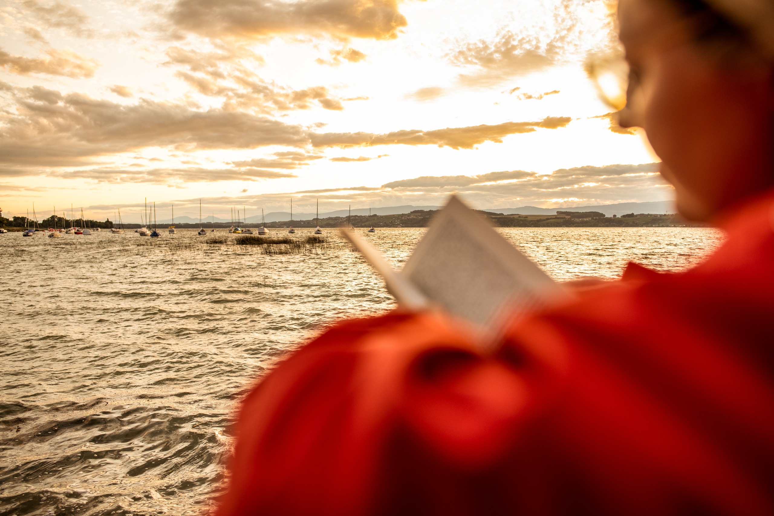 Frau mit Rotem Regenmantel am See. Frau liest am See ein Buch, stürmisches Wetter