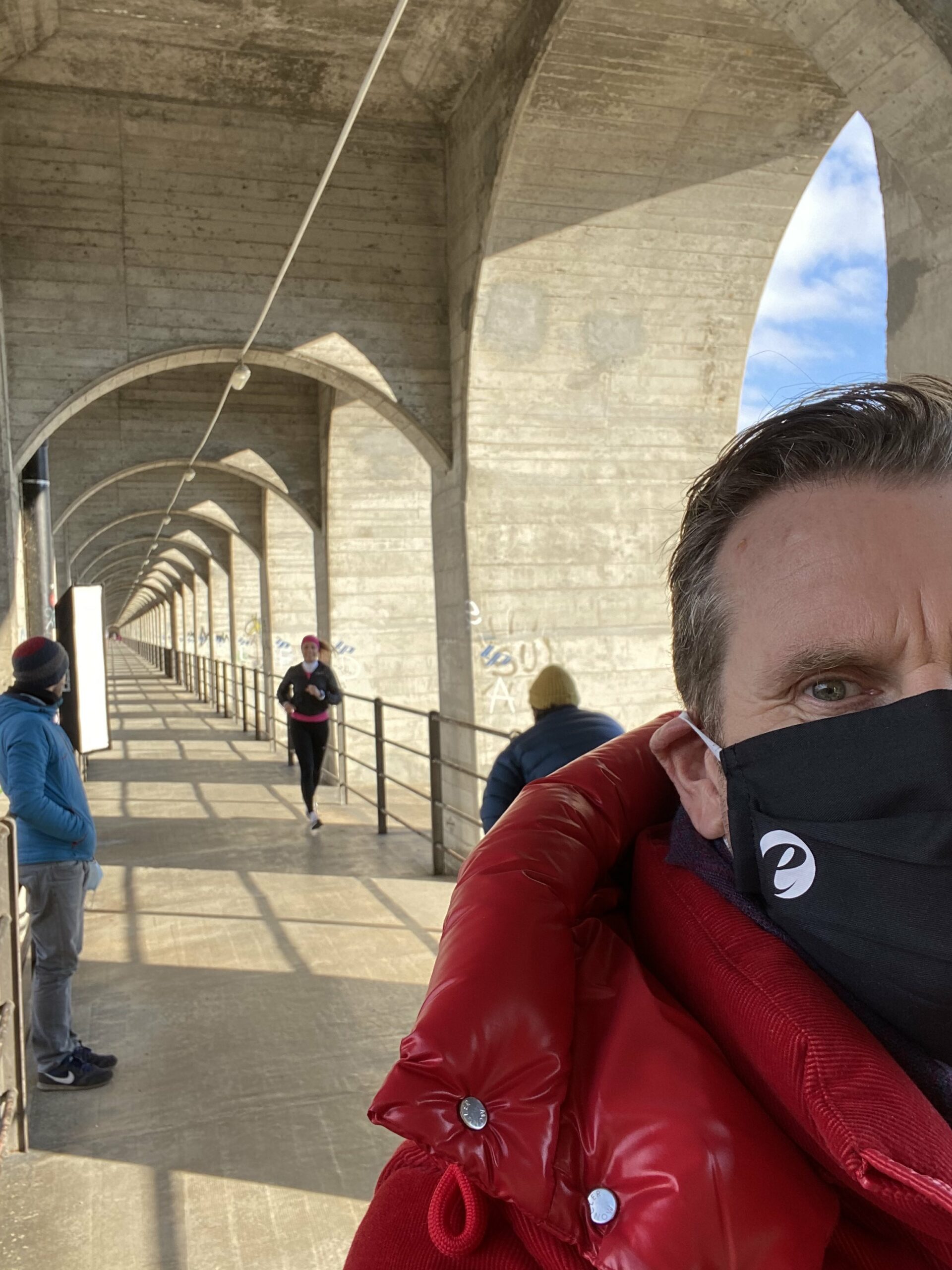 Grand Fey Br&uuml;cke mit Joggerin und Kamera Team. Mann im Vordergrund mit roter Jacke.
