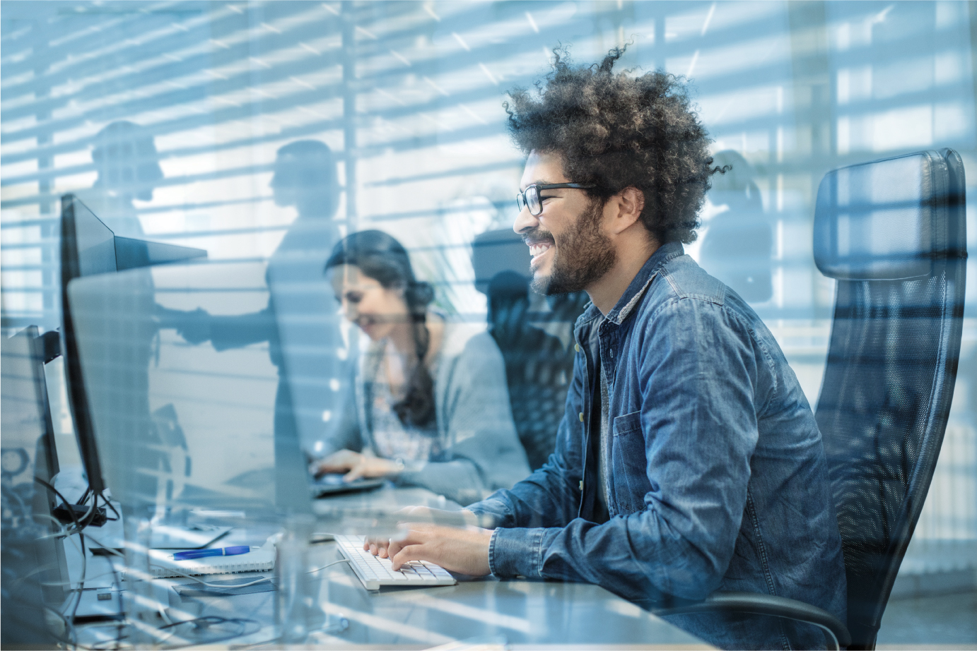IT-Programmier mit Spiegelungseffekt im Blauton. Mann vor dem Computer mit krausem Haar.