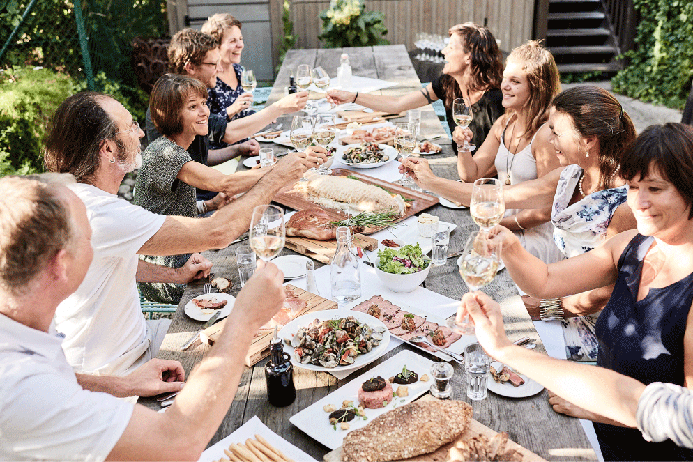 Menschen sitzen auf der Gartenterasse und stossen mit Wein an.