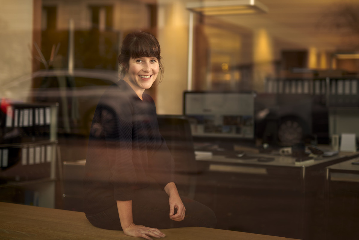 Frau sitzt im Büro mit Spiegelungseffekten. Aufnahme durch das Fenster.