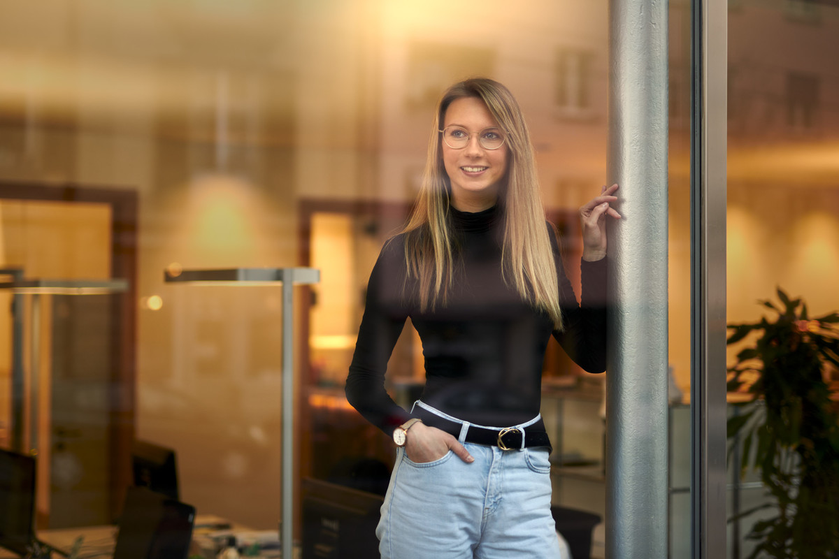 Frau steht im Büro mit Spiegelungseffekten. Aufnahme durch das Fenster.
