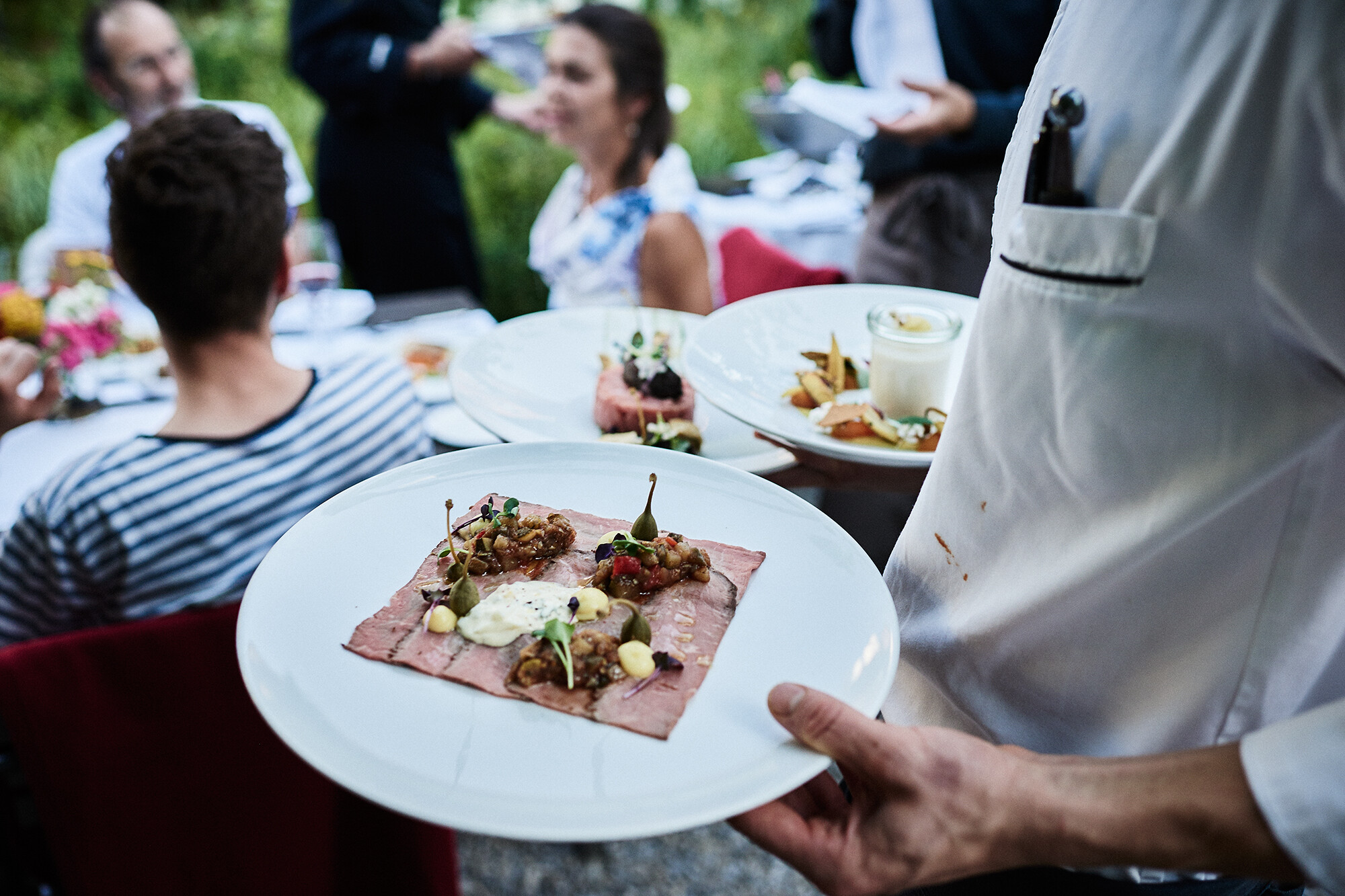 Haberbüni Restaurant Service, Kellner i Garten mit zwei Tellern.