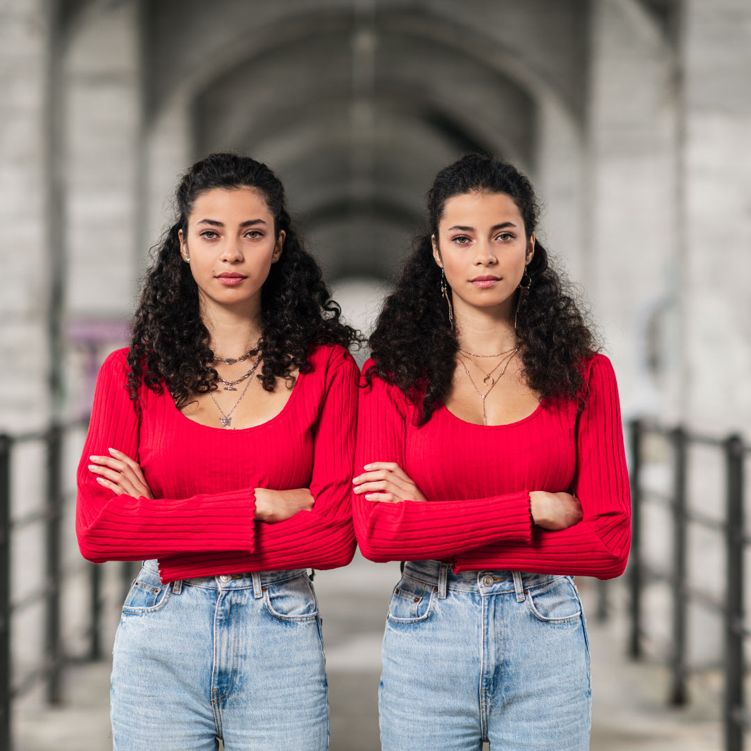 Zwillinge im roten Cropt-Shirt stehen in einer Unterführung. Junge Zwillinge mit krausem Haar posen unter der Grandfey Brücke.