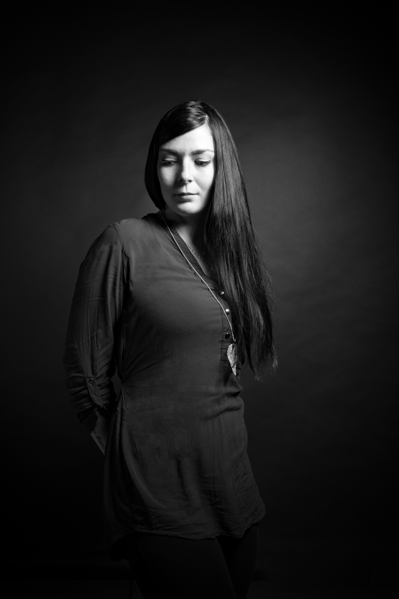 Frau mit langen dunklen Haaren vor dunklem Hintergrund in dunkler Kleidung.