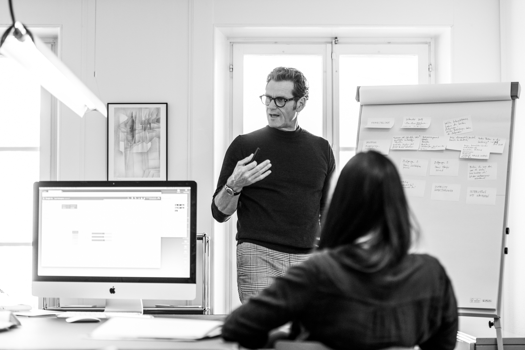 Thierry Laillard steht vor Flipchart und spricht mit Mitarbeitern. Internes Brainstorming. Frau von Hinten auf dem Stuhl während einer Besprechung.