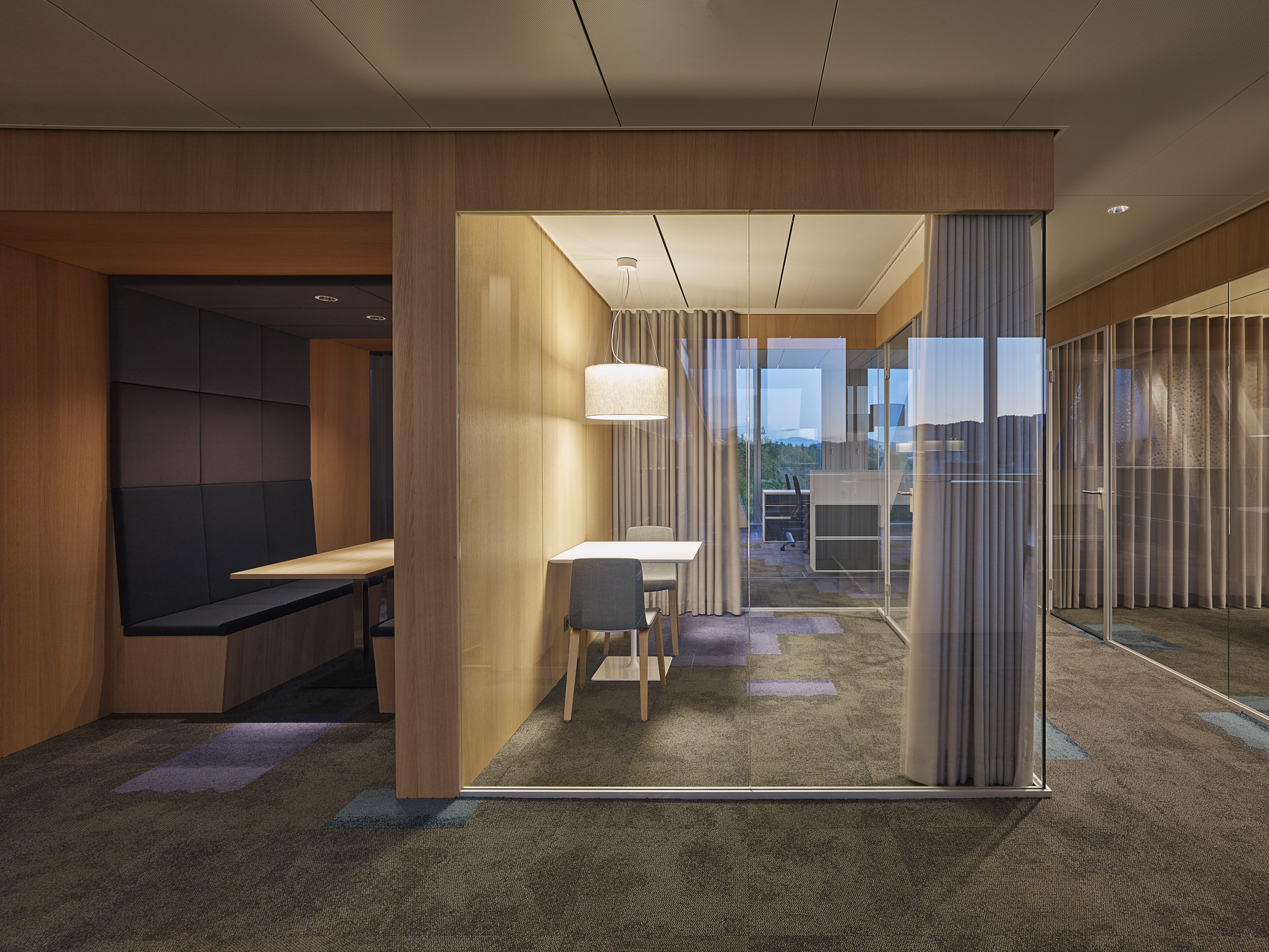 Büro Ecke offen mit dunklen Violetten Bezügen auf Bänken. Glas Büro mit Vorhängen und runder Leuchte.