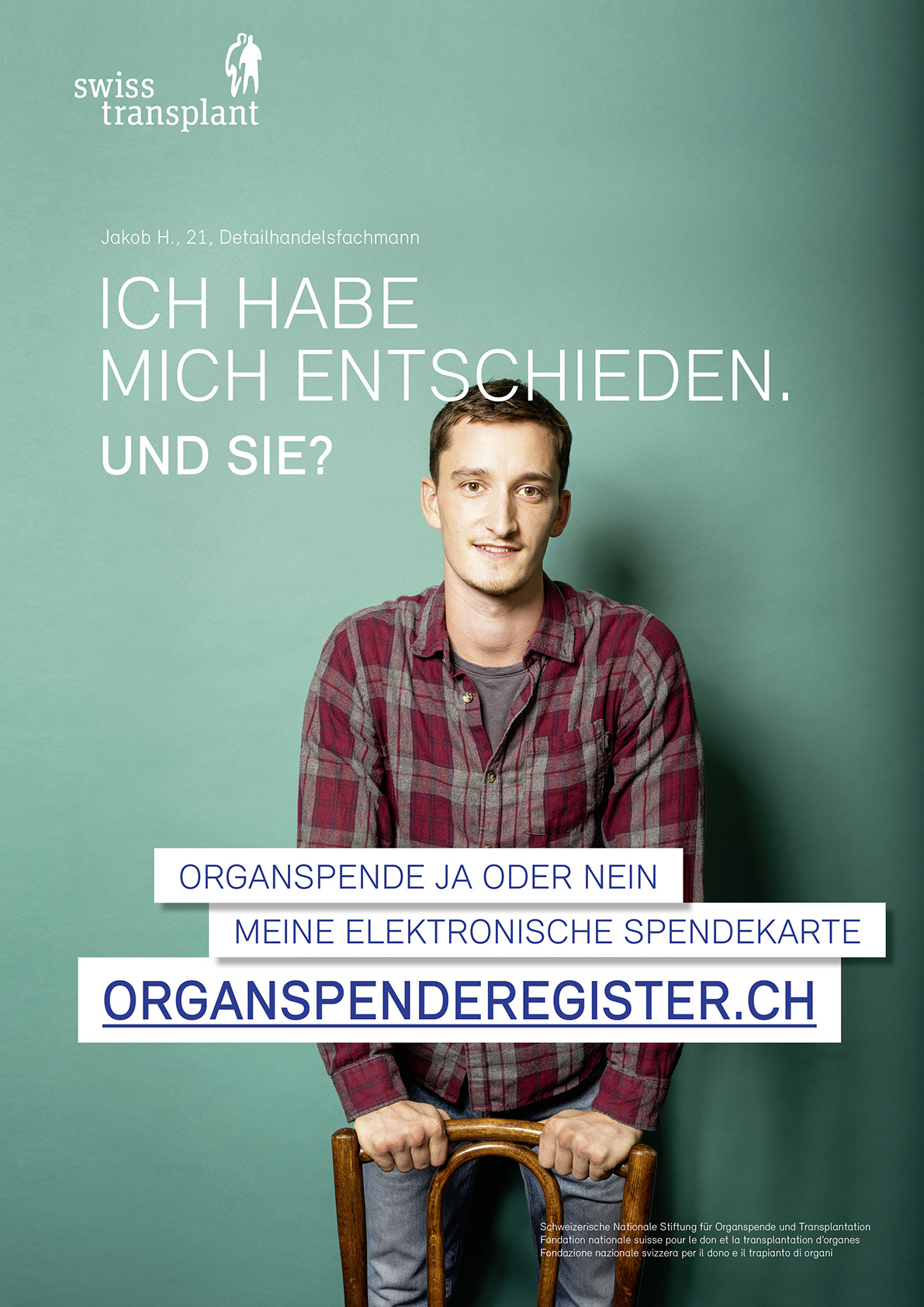 Junger Mann mit Karierten Hemd steht vor gr&uuml;ner Wand. Statement zur Organspende in Buchbinden.