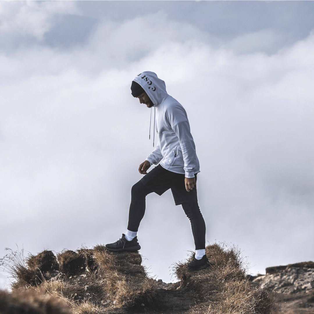 Mann steht auf den Dolomiten in Italien mit Pullover und Kapuze. Mann im weissen Pullover von Kaiman.