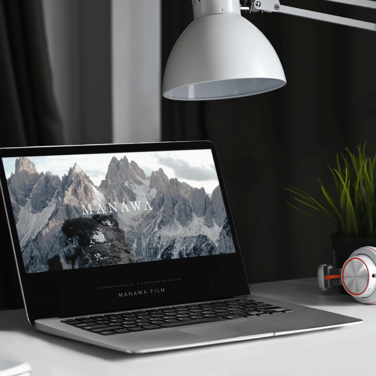 Laptop stehend auf dem Tisch mit Webseite von MANAWA Film geöffnet. Lampe und Kopfhörer stehen mit Laptop auf Schreibtisch.