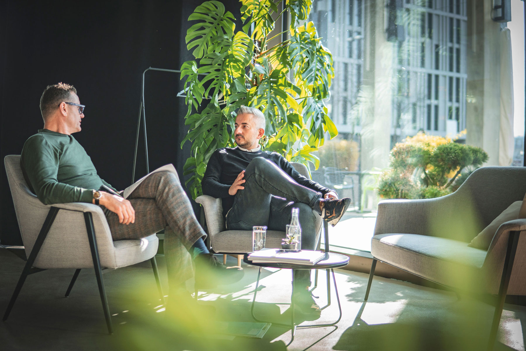 Roland Schaad im Interview mit Thierry Laillard. Zwei Männer sitzen in einem Hotel und reden zwischen vielen grünen Pflanzen.