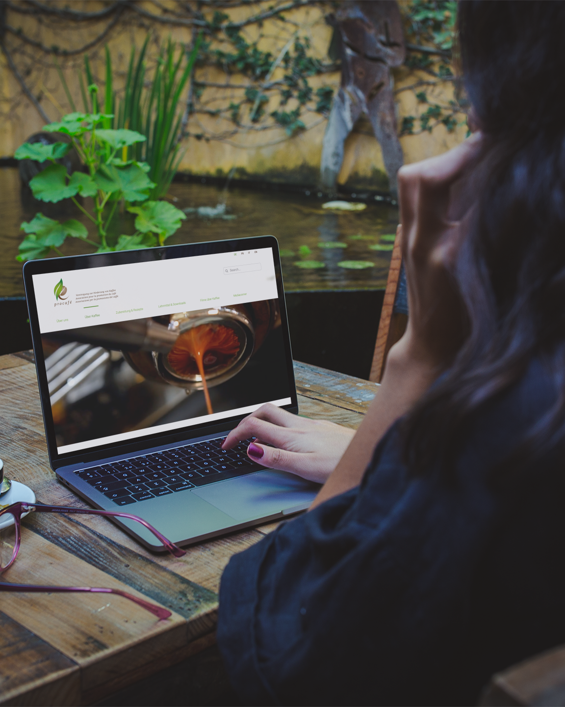 Frau sieht sich in einem schönen grünen Oase die Procafé Website mit einem Kaffee auf dem Tisch an. Webdesign für Procafé