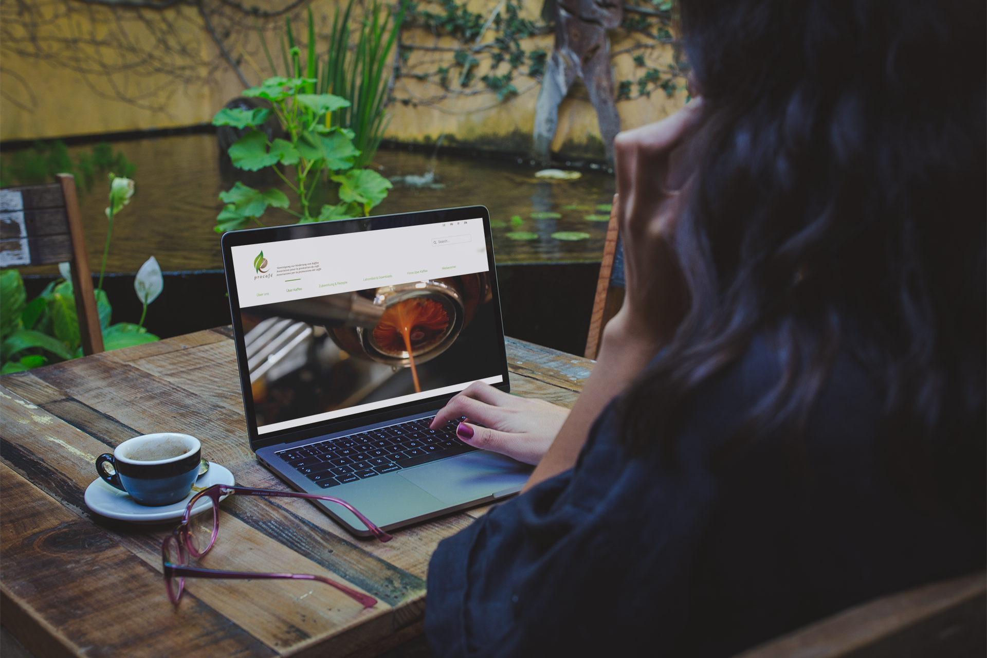 Frau sieht sich in einem schönen grünen Oase die Procafé Website mit einem Kaffee auf dem Tisch an. Webdesign für Procafé
