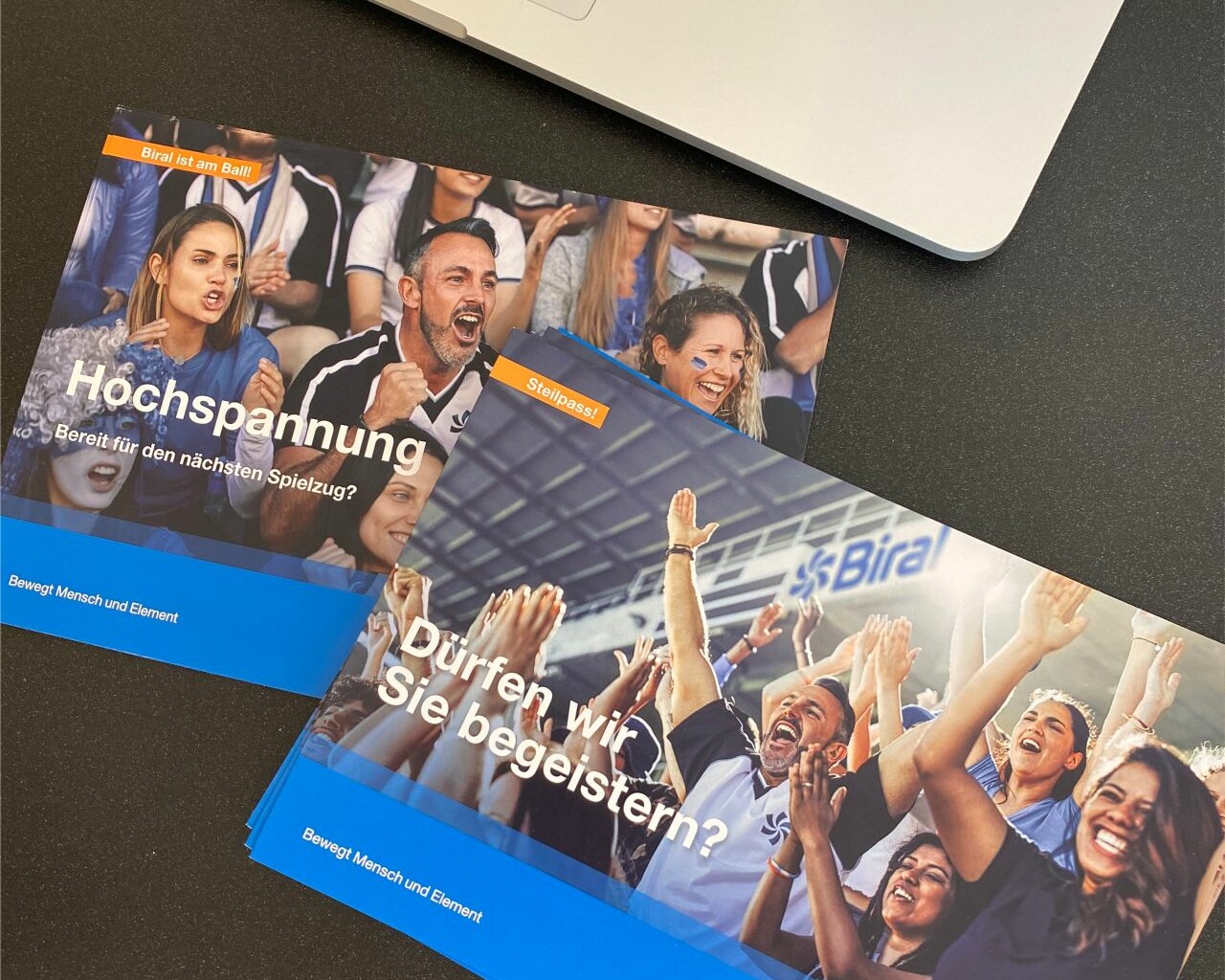 Dürfen wir Sie begeistern? Mailing Biral liegend auf dem Tisch neben MAC Book