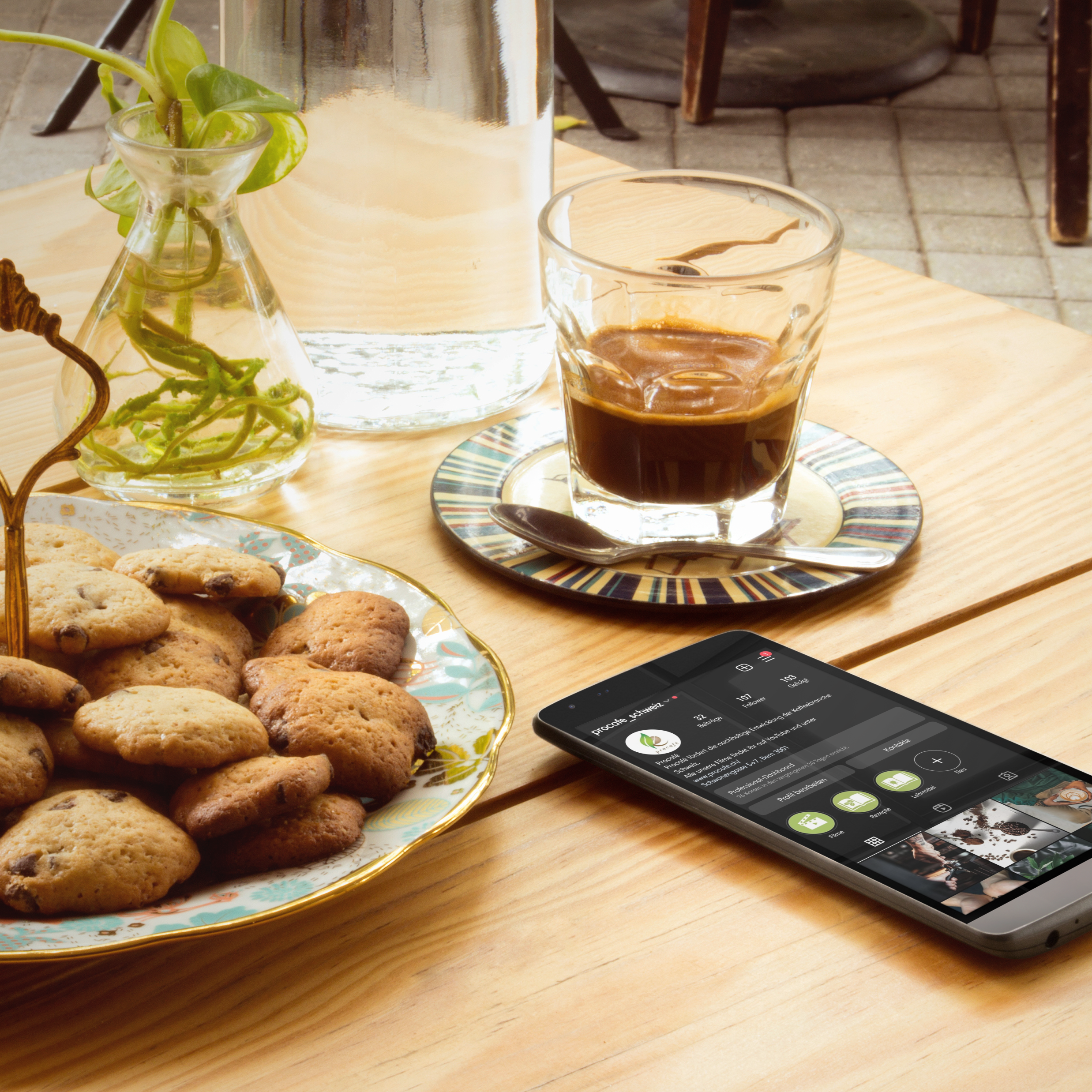 Handy liegt auf einem Holztisch neben einem Kaffee und Keksen