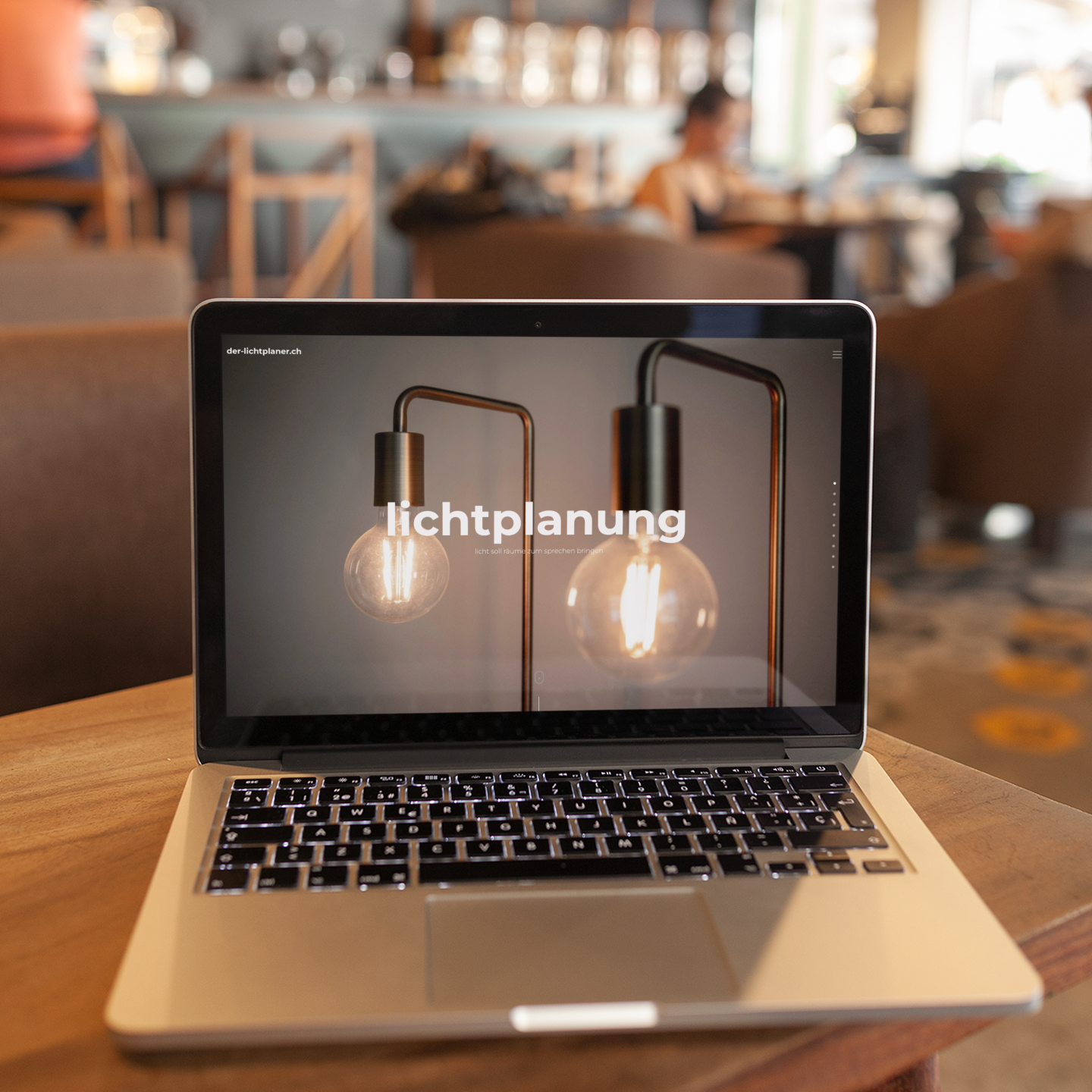 Laptop steht auf einem Holztisch und zeigt eine Seite von der-lichtplaner. Im Hintergrund ist ein Caff&eacute; verschwommen.
